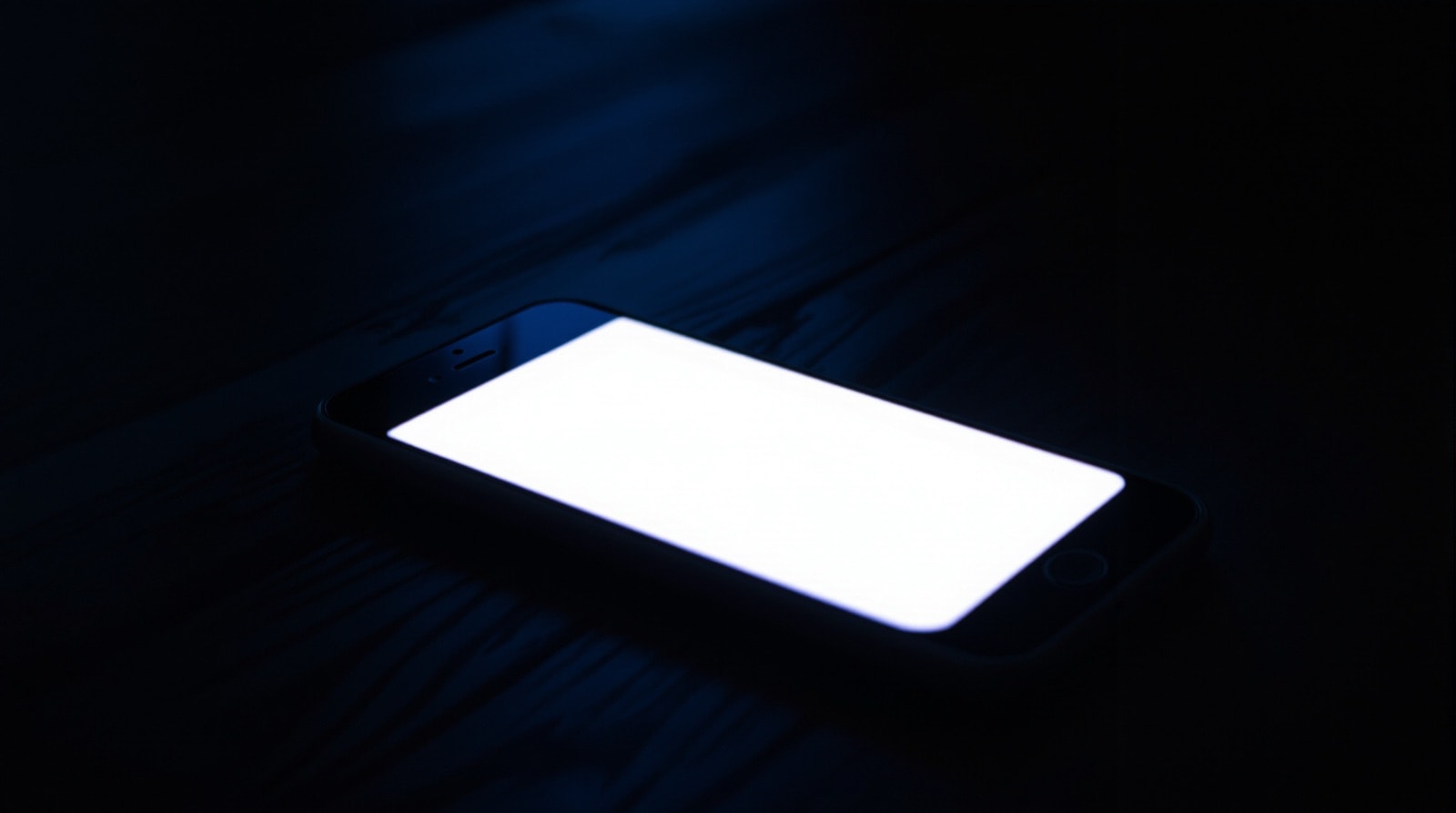A phone screen glowing in a darkened room showing a bright blank message overlay